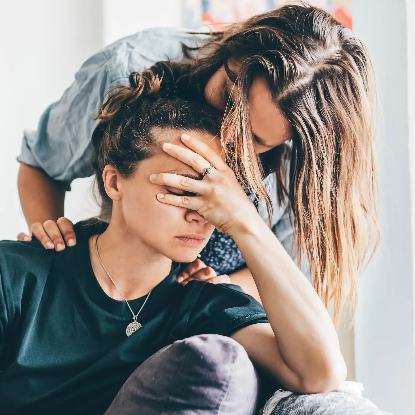 Eine Frau beugt sich über ihre Partnerin, die sich die Hand vors Gesicht hält